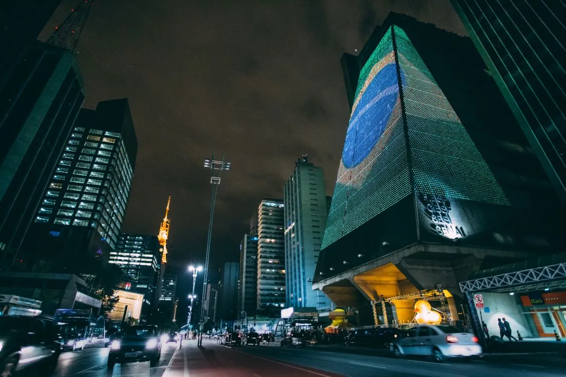 Cars traveling along an urban avenue at night between tall buildings, illustrating driving conditions on the São Paulo–Rio corridor.