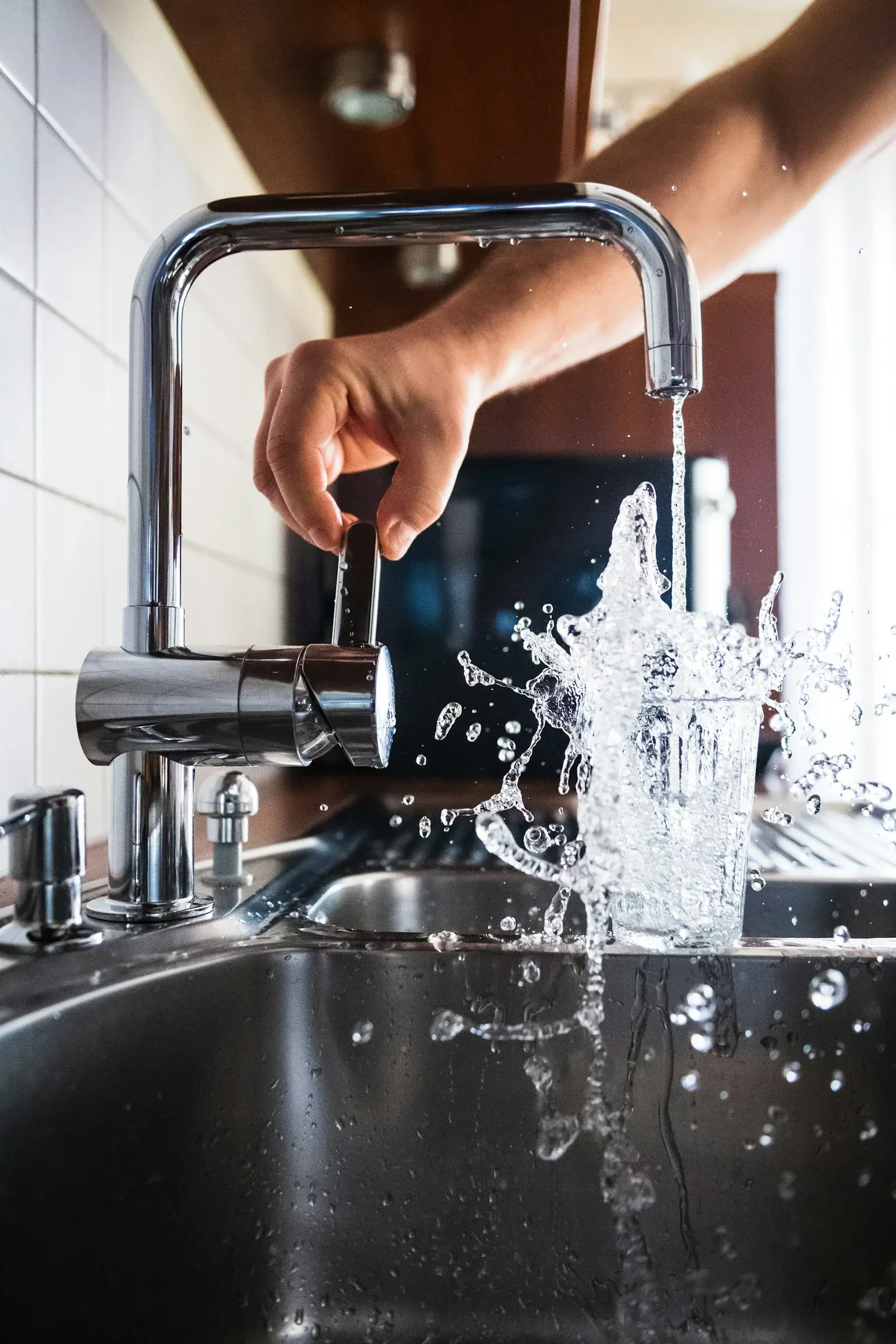 A clear glass of water being filled at a modern kitchen tap, representing tap water safety in Brazil